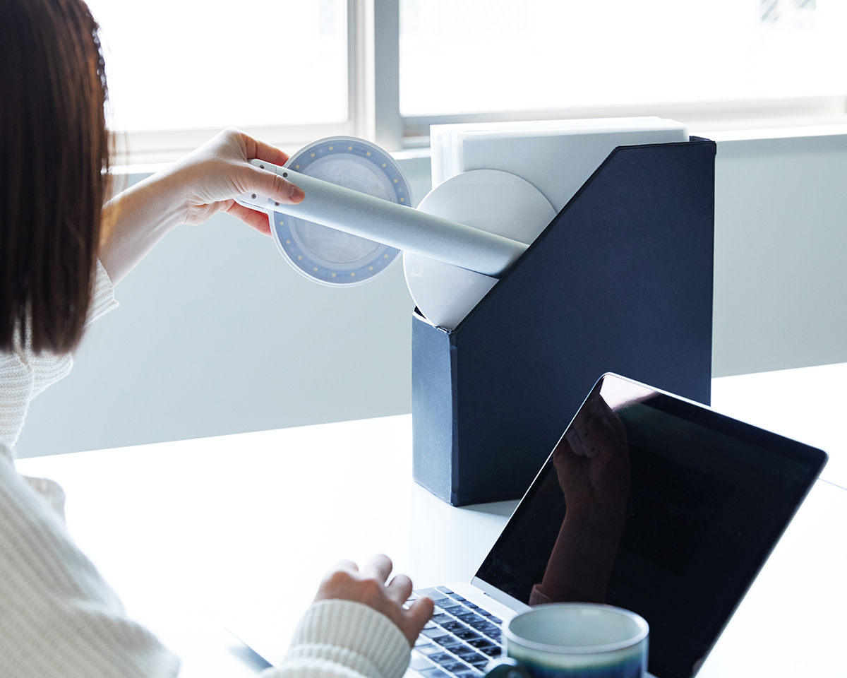 書類ボックスの隙間にコンパクトに収納できる。コードレスで使えて、薄さ4cmにたためる、手元を大きく・明るく照らすルーペ付き太陽光LEDの「デスクライト」|daylight - Halo Go